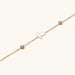 Gold chain bracelet with white mother of pearl butterfly pendant and two bezel-set crystals on cream background