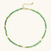 Layered necklace with green stone beads, gold spacers, white accents, and protective eye pendant on cream background.