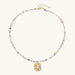 Ornate gold-plated pendant necklace with multicolored gemstone beads in purple, pink and clear tones on white background