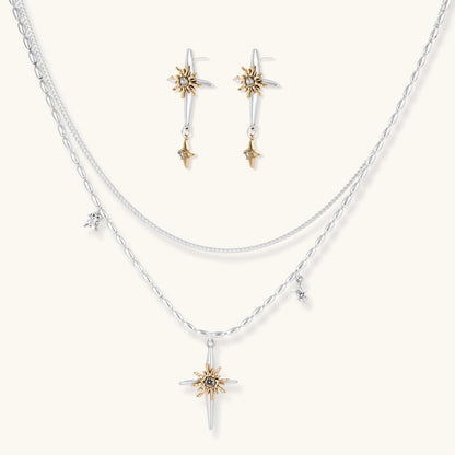 Layered silver-toned necklace set with cross pendant and gold sun charm detail, matching drop earrings on white background.