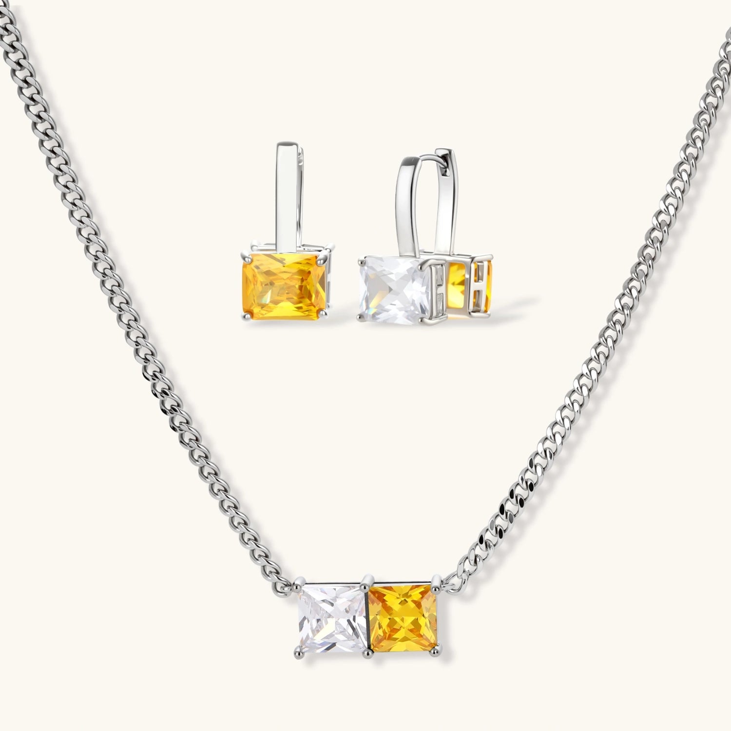 Silver curb-chain necklace and hoop drop earrings set with paired yellow and clear square zirconia stones.