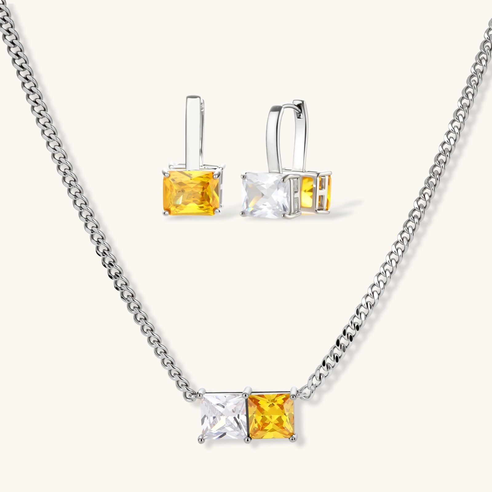 Silver curb-chain necklace and hoop drop earrings set with paired yellow and clear square zirconia stones.