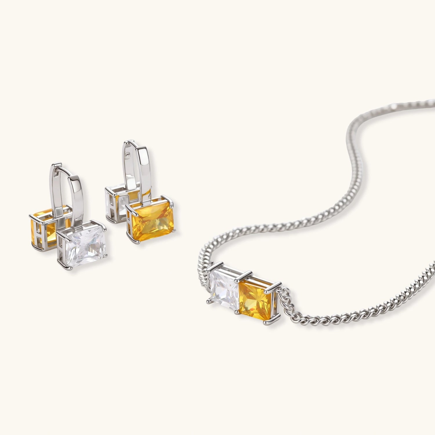 Silver curb-chain necklace and hoop drop earrings set with paired yellow and clear square zirconia stones.