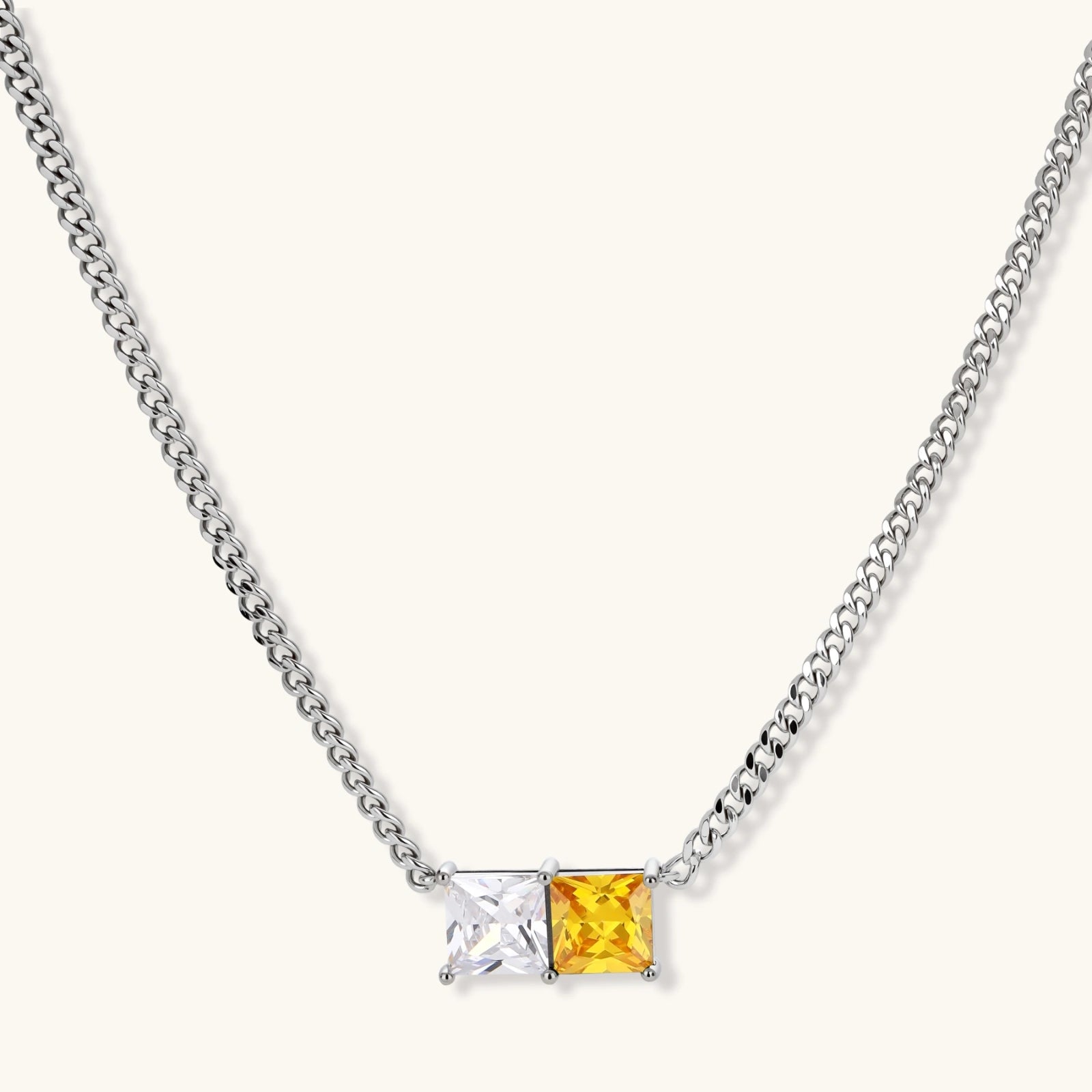 Silver curb-chain necklace and hoop drop earrings set with paired yellow and clear square zirconia stones.
