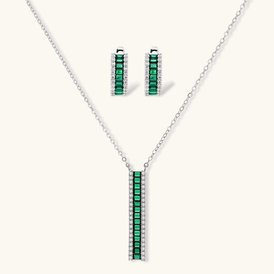 White gold plated jewelry set with emerald green rectangular stones and clear crystals in geometric rows on white background.