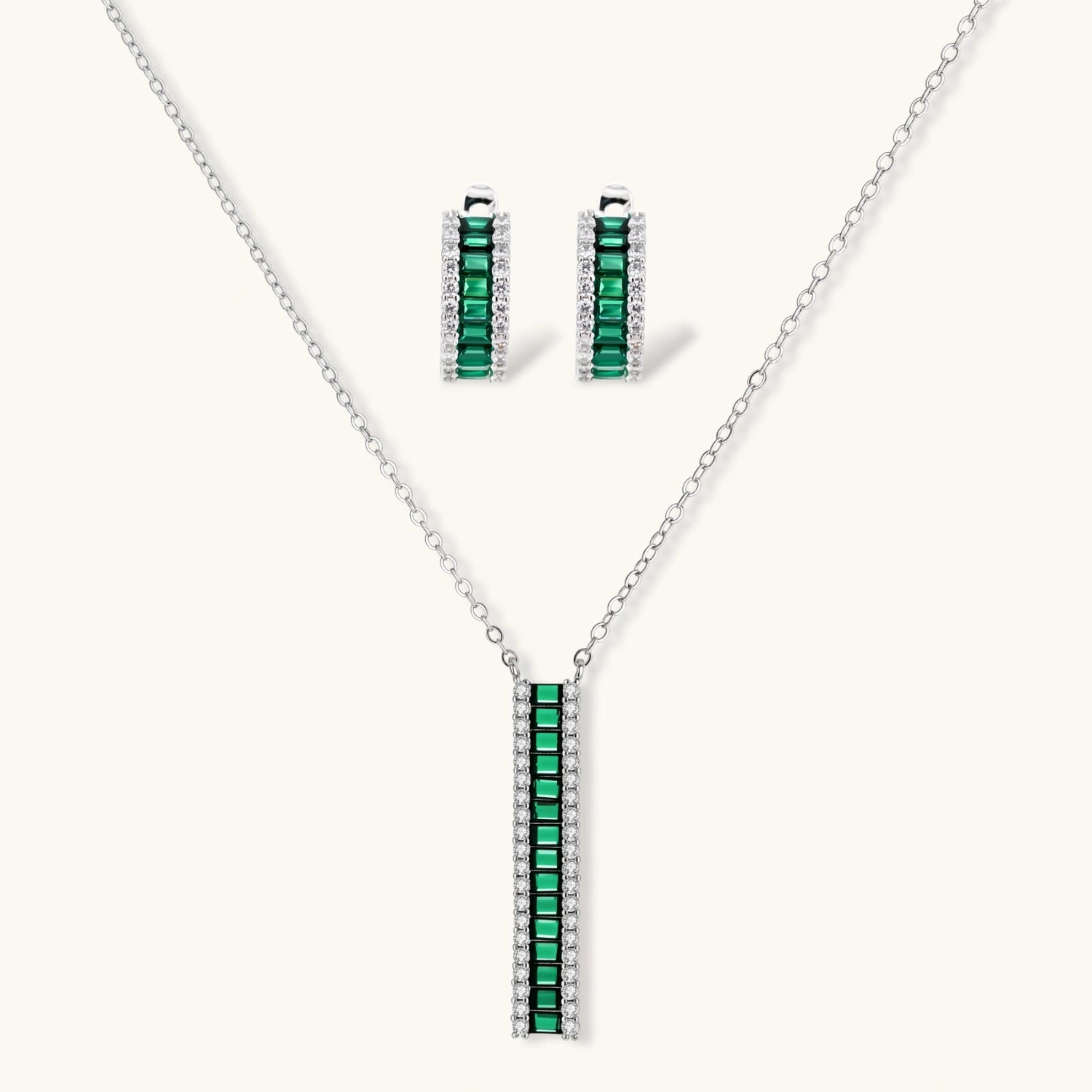 White gold plated jewelry set with emerald green rectangular stones and clear crystals in geometric rows on white background.