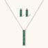 White gold plated jewelry set with emerald green rectangular stones and clear crystals in geometric rows on white background.