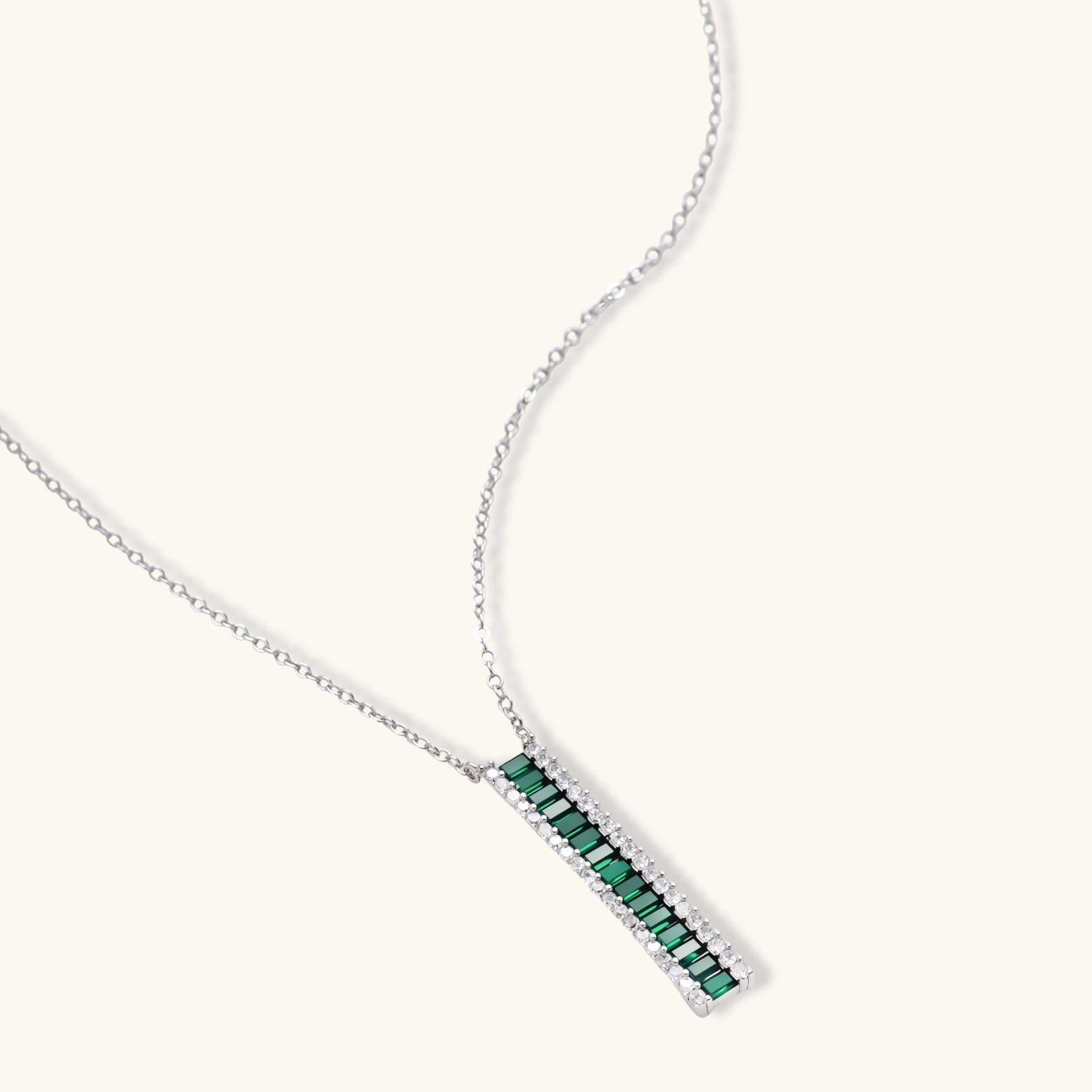 White gold plated jewelry set with emerald green rectangular stones and clear crystals in geometric rows on white background.