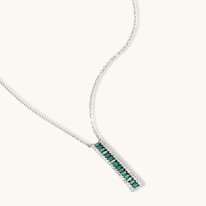 White gold plated jewelry set with emerald green rectangular stones and clear crystals in geometric rows on white background.