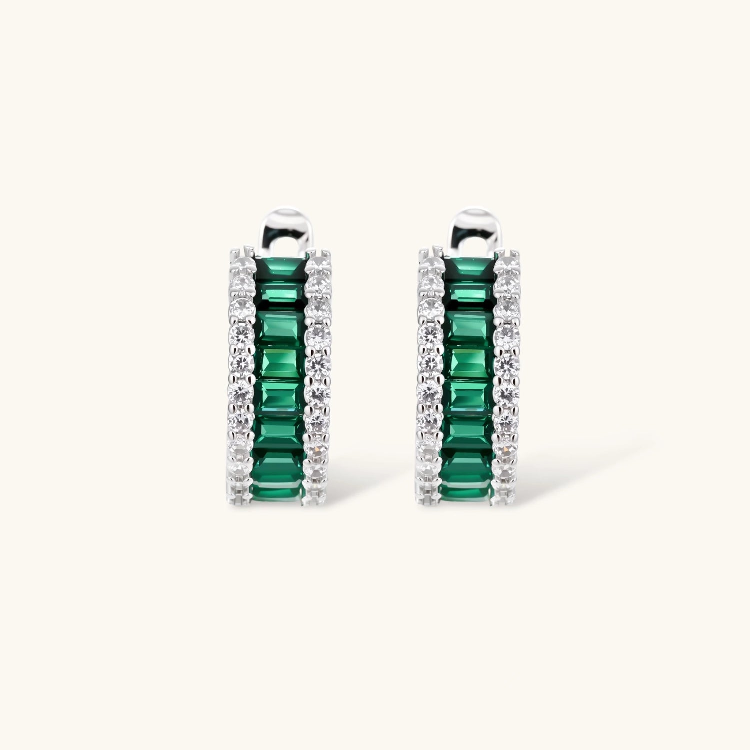 White gold plated jewelry set with emerald green rectangular stones and clear crystals in geometric rows on white background.