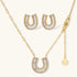Gold-plated horseshoe necklace and earring set with baguette and round crystals arranged in geometric pattern on white background.