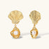 Gold shell-shaped drop earrings with scallop tops and oyster bottoms featuring round freshwater pearls on white background.